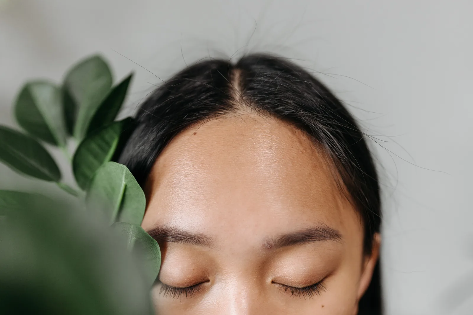 Mulher com raiz do cabelo à mostra perto de folhas verdes