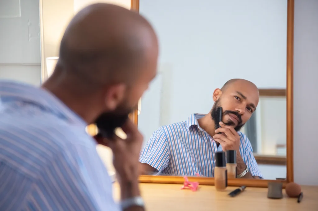 Homem aparando a barba em frente ao espelho