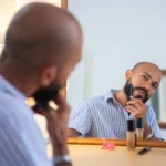Homem aparando a barba em frente ao espelho