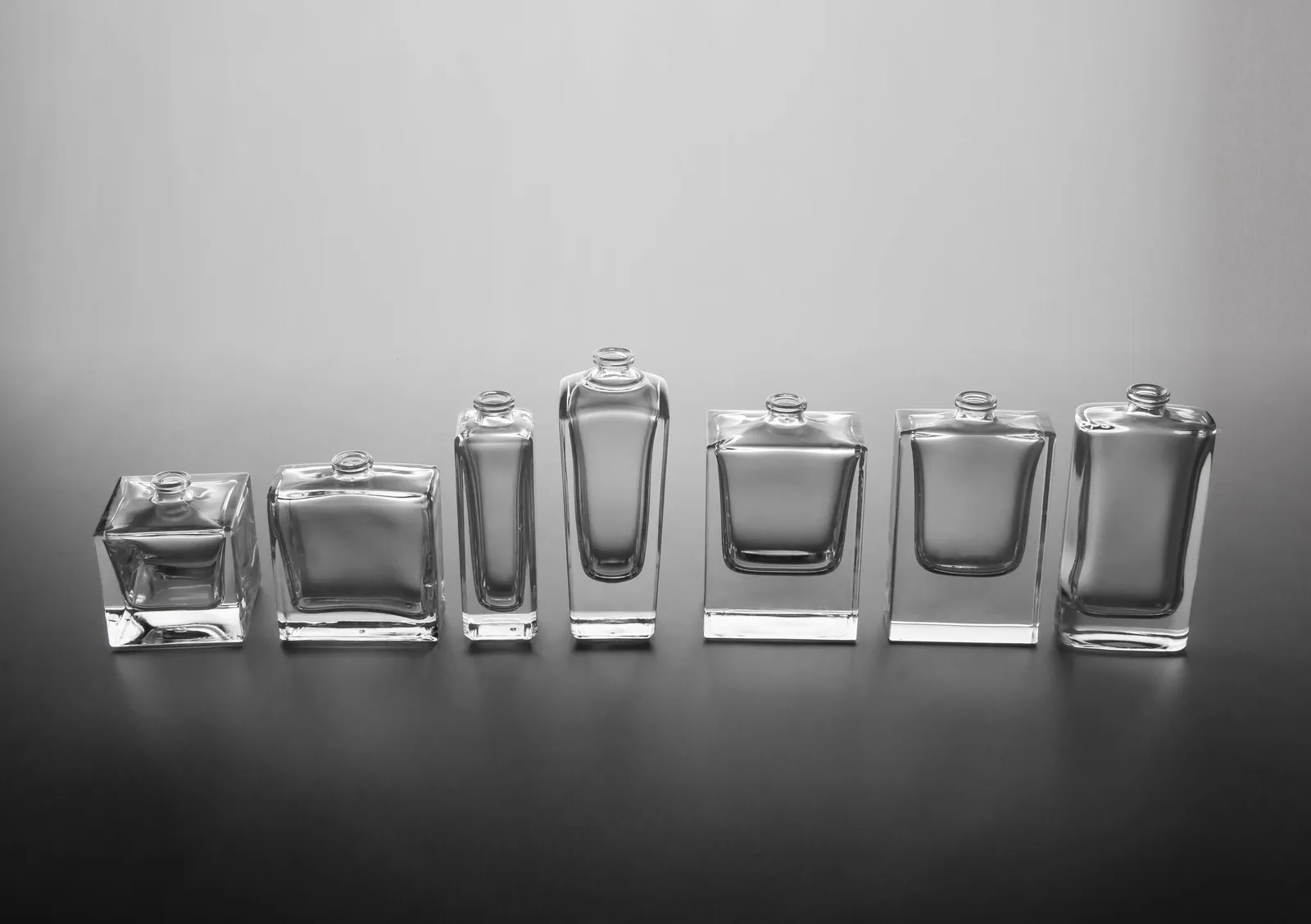 Sete frascos de perfume de tamanhos diferentes enfileirados (EDT, EDP, parfum)