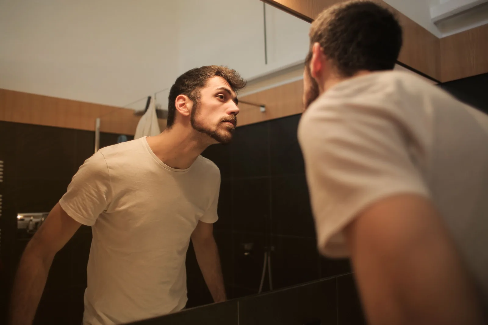 Homem observando a linha do cabelo no espelho do banheiro